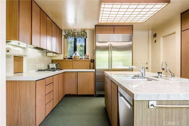 kitchen with appliances with stainless steel finishes, sink, backsplash, and an island with sink