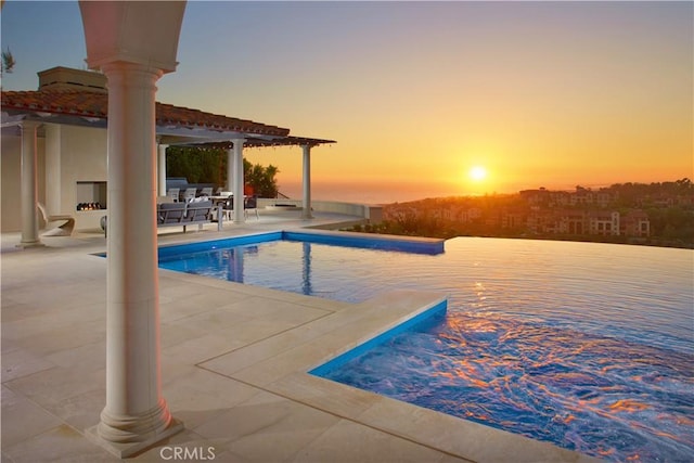 pool at dusk with an outdoor fireplace and a patio