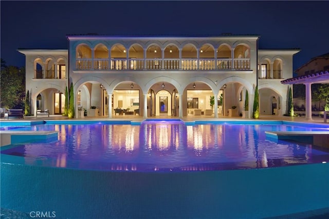 back house at night featuring a balcony and a patio area