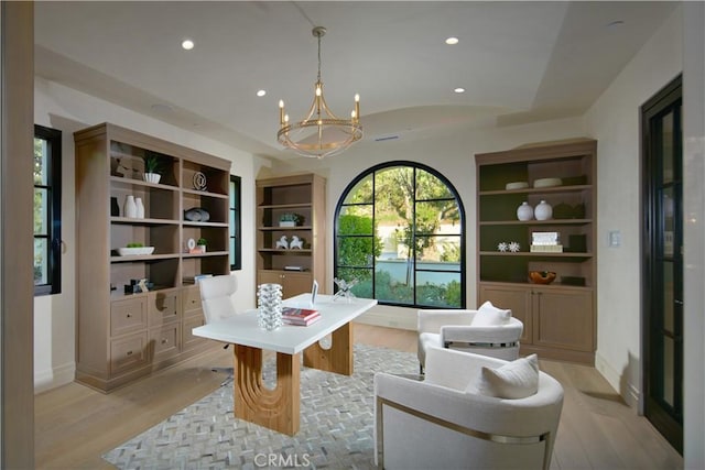 home office featuring lofted ceiling, an inviting chandelier, built in features, and light hardwood / wood-style floors