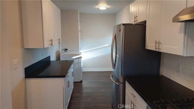 kitchen with dark wood-style flooring, white cabinets, wall chimney exhaust hood, dark countertops, and tasteful backsplash