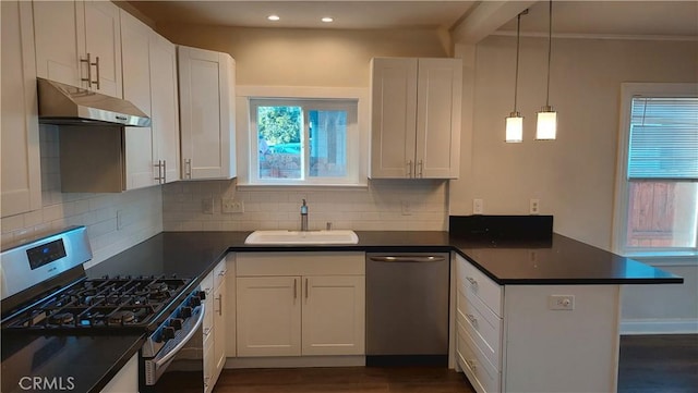 kitchen with a peninsula, stainless steel appliances, dark countertops, under cabinet range hood, and a sink