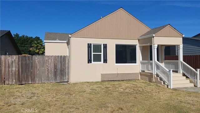 view of front of property with a shingled roof, a front yard, fence, and stucco siding