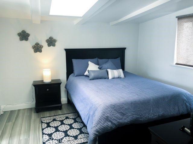 bedroom featuring beam ceiling, hardwood / wood-style flooring, and a skylight