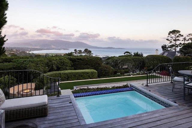 pool at dusk featuring a deck with water view