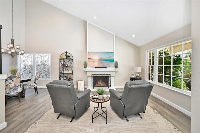 living room featuring light hardwood / wood-style floors, a fireplace, high vaulted ceiling, and a chandelier