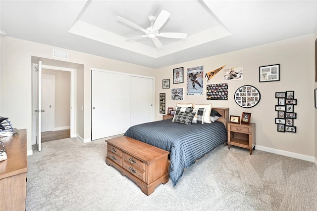 carpeted bedroom with ceiling fan, a raised ceiling, and a closet