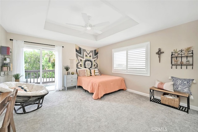 carpeted bedroom with access to exterior, a tray ceiling, and ceiling fan