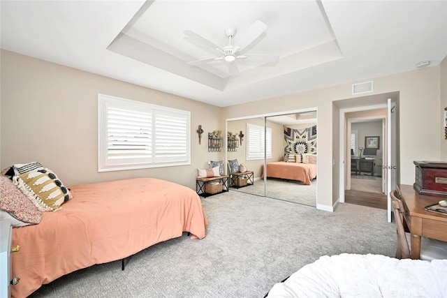 carpeted bedroom featuring a raised ceiling, a closet, and ceiling fan