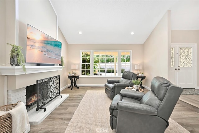 living room with a fireplace, vaulted ceiling, and light wood-type flooring