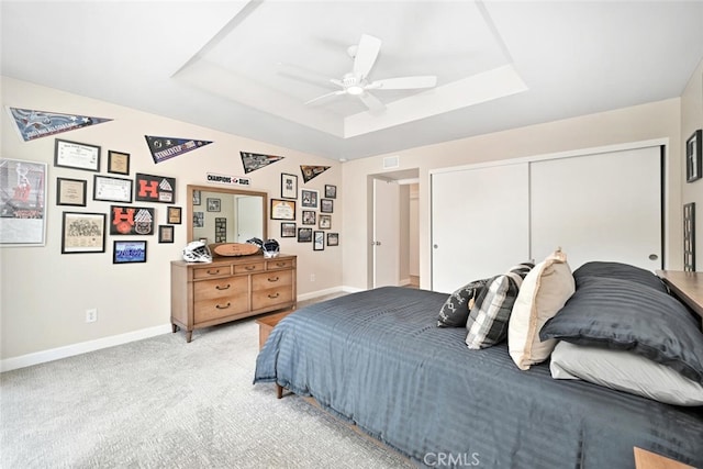 bedroom with ceiling fan, a raised ceiling, light carpet, and a closet