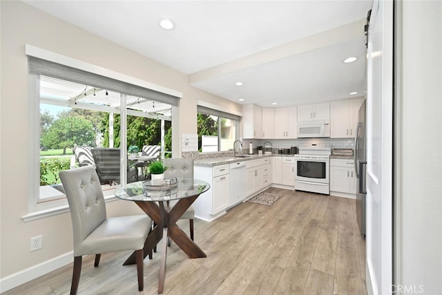 kitchen featuring light wood-type flooring, tasteful backsplash, white appliances, sink, and white cabinets