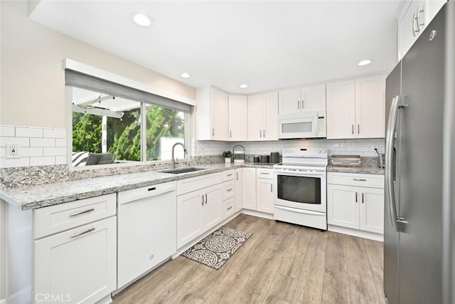 kitchen with white appliances, sink, light hardwood / wood-style flooring, light stone counters, and white cabinetry