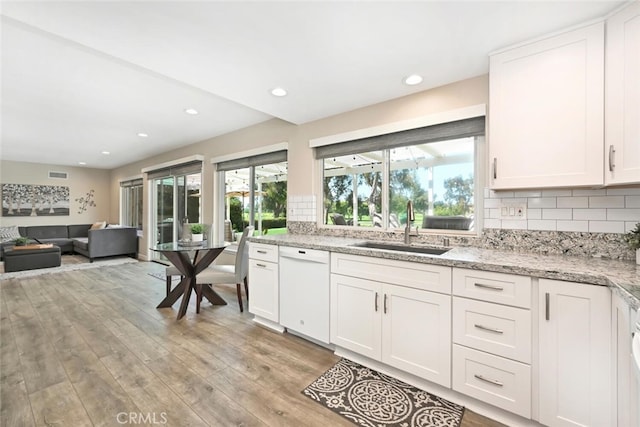 kitchen with white cabinets, dishwasher, light stone counters, and light hardwood / wood-style flooring