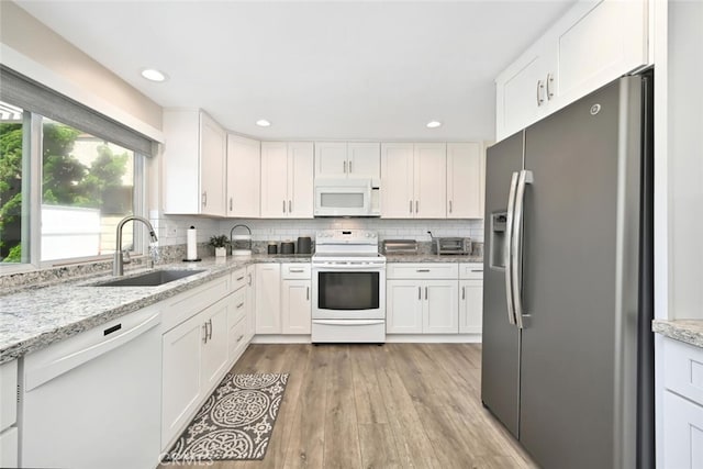 kitchen with white appliances, sink, light hardwood / wood-style flooring, light stone countertops, and white cabinetry