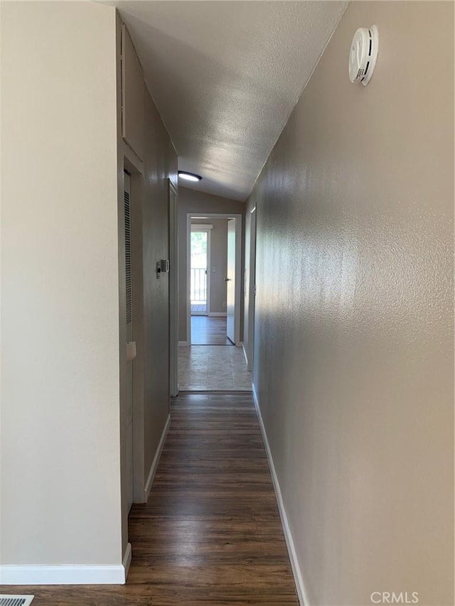 hall with vaulted ceiling, dark hardwood / wood-style flooring, and a textured ceiling