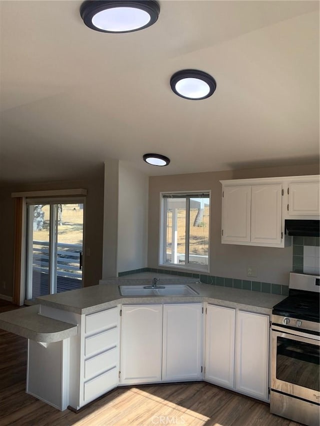 kitchen featuring kitchen peninsula, sink, light wood-type flooring, stainless steel gas range, and white cabinets