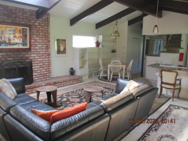 living room with vaulted ceiling with beams and a brick fireplace