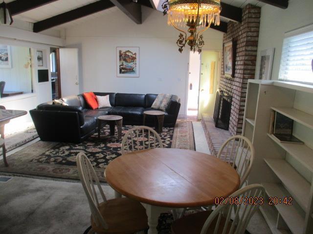 dining room with vaulted ceiling with beams, a chandelier, and a brick fireplace