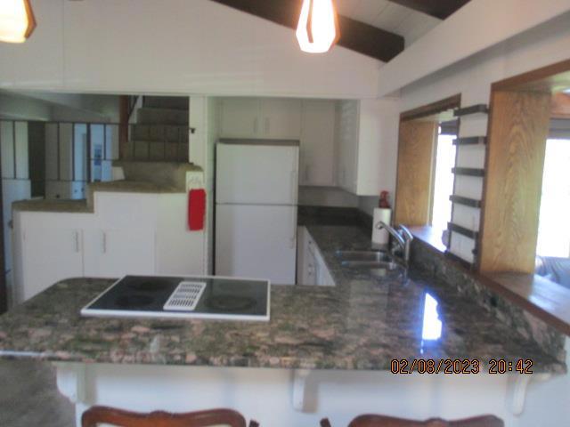 kitchen featuring kitchen peninsula, cooktop, white fridge, and sink