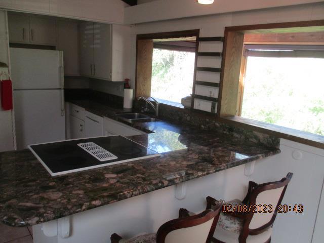 kitchen featuring kitchen peninsula, dark stone countertops, sink, white refrigerator, and electric cooktop