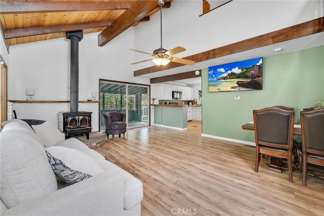 living room with a wood stove, ceiling fan, beam ceiling, wood ceiling, and light hardwood / wood-style flooring