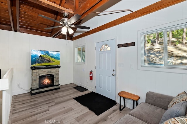 entrance foyer featuring ceiling fan, light hardwood / wood-style flooring, wooden ceiling, beam ceiling, and a stone fireplace