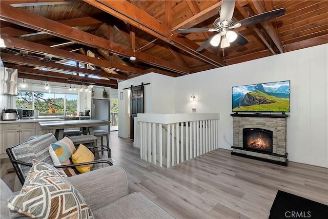 sitting room featuring ceiling fan, light hardwood / wood-style floors, wooden ceiling, a barn door, and lofted ceiling with beams