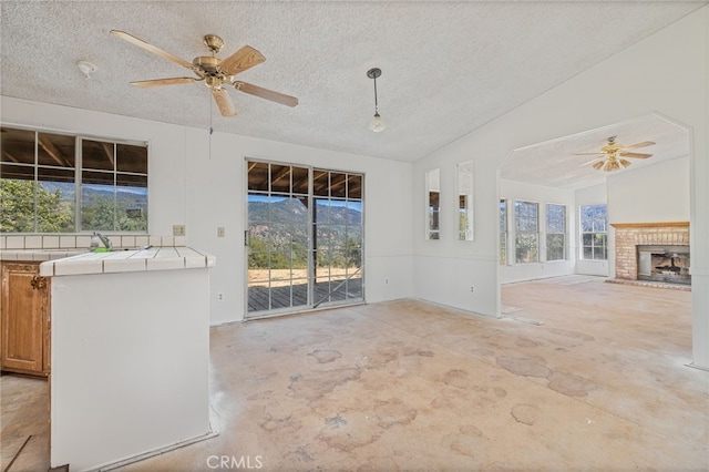 unfurnished living room with a healthy amount of sunlight, ceiling fan, lofted ceiling, and a textured ceiling