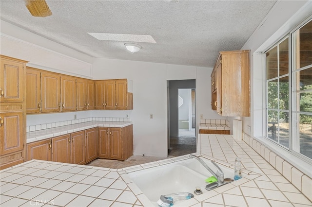 kitchen featuring a textured ceiling, tile countertops, and vaulted ceiling with skylight