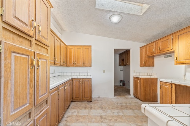 kitchen with tile countertops, lofted ceiling with skylight, and a textured ceiling