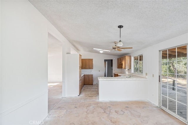 kitchen with tile countertops, lofted ceiling, ceiling fan, kitchen peninsula, and a textured ceiling