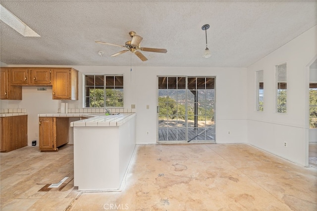 kitchen with tile countertops, a skylight, hanging light fixtures, and a textured ceiling