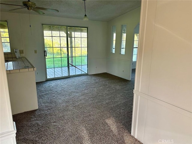 unfurnished living room with dark carpet, a wealth of natural light, a textured ceiling, and vaulted ceiling