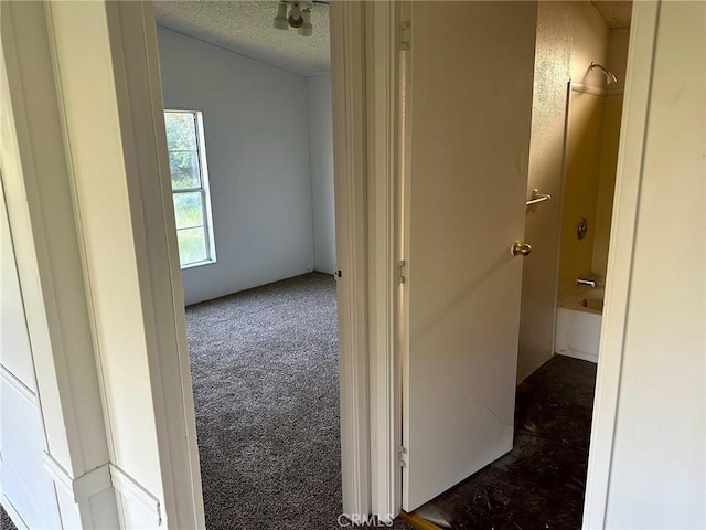 hallway with dark colored carpet and a textured ceiling