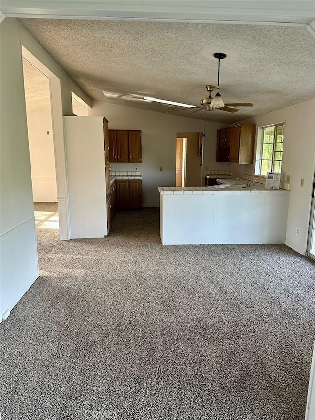 kitchen featuring ceiling fan, tile counters, a textured ceiling, light carpet, and kitchen peninsula