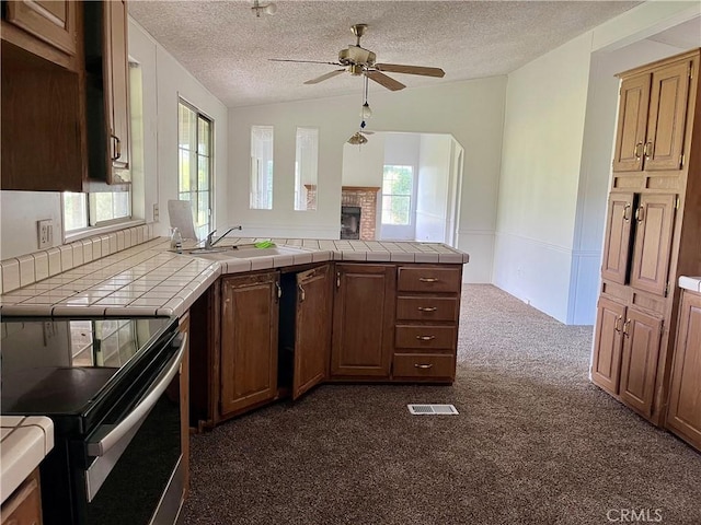 kitchen featuring lofted ceiling, sink, a textured ceiling, electric range, and tile counters