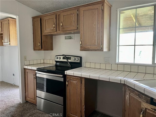 kitchen featuring dark carpet, tile countertops, stainless steel range with electric cooktop, and a textured ceiling