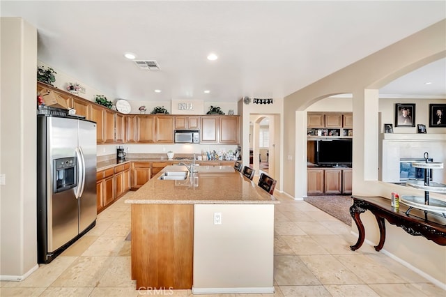 kitchen featuring a center island with sink, appliances with stainless steel finishes, light tile floors, and light stone counters