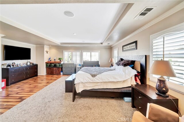 bedroom featuring a tray ceiling, ornamental molding, light wood-type flooring, and a tiled fireplace