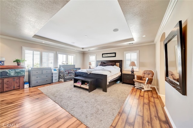 bedroom with crown molding, hardwood / wood-style floors, a tray ceiling, and a textured ceiling