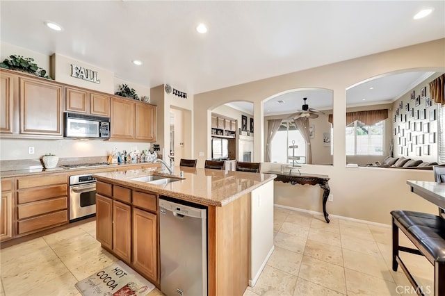 kitchen featuring an island with sink, stainless steel appliances, light stone countertops, ceiling fan, and sink