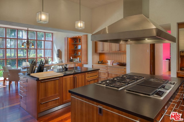 kitchen with hanging light fixtures, a center island, ventilation hood, stainless steel gas cooktop, and dark hardwood / wood-style flooring