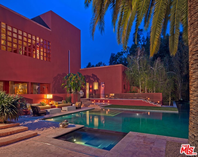 pool at night featuring an in ground hot tub and a patio