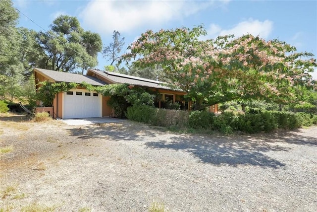 view of front facade featuring an attached garage, solar panels, and gravel driveway