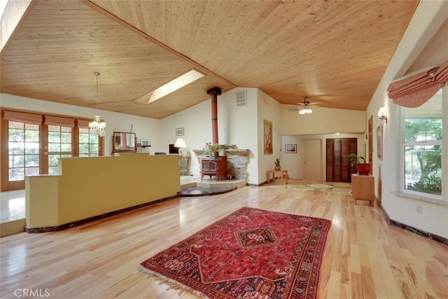 interior space with a skylight, ceiling fan with notable chandelier, a wood stove, and visible vents