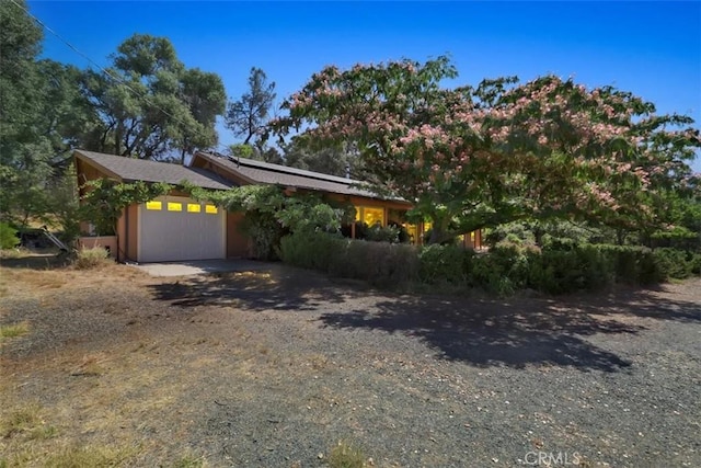 view of front of property with dirt driveway, an attached garage, and roof mounted solar panels