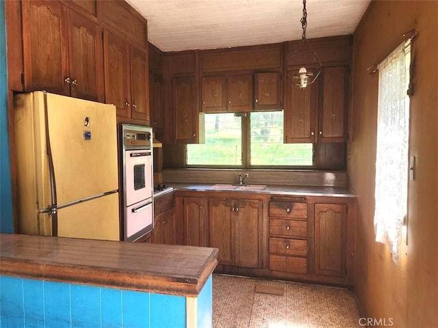 kitchen featuring pendant lighting, white appliances, brown cabinetry, a warming drawer, and a sink