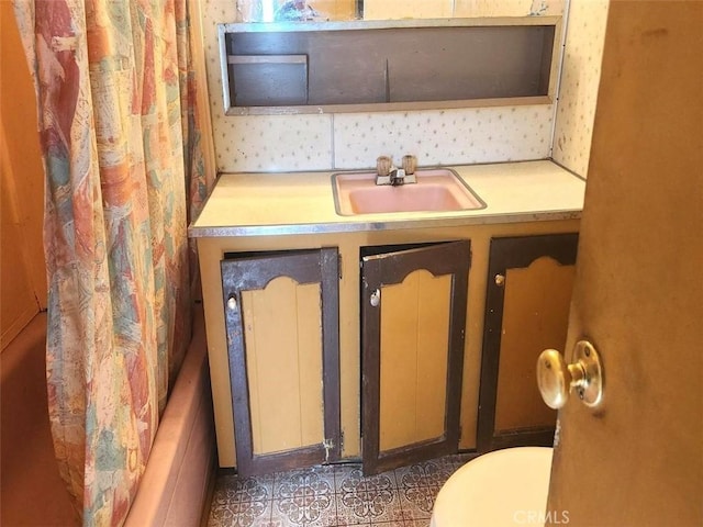 bathroom with wallpapered walls, a bathtub, a sink, and toilet