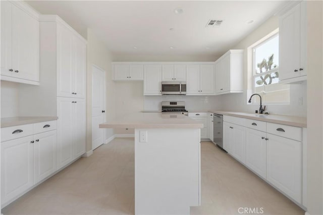 kitchen with stainless steel appliances, white cabinetry, a kitchen island, and sink